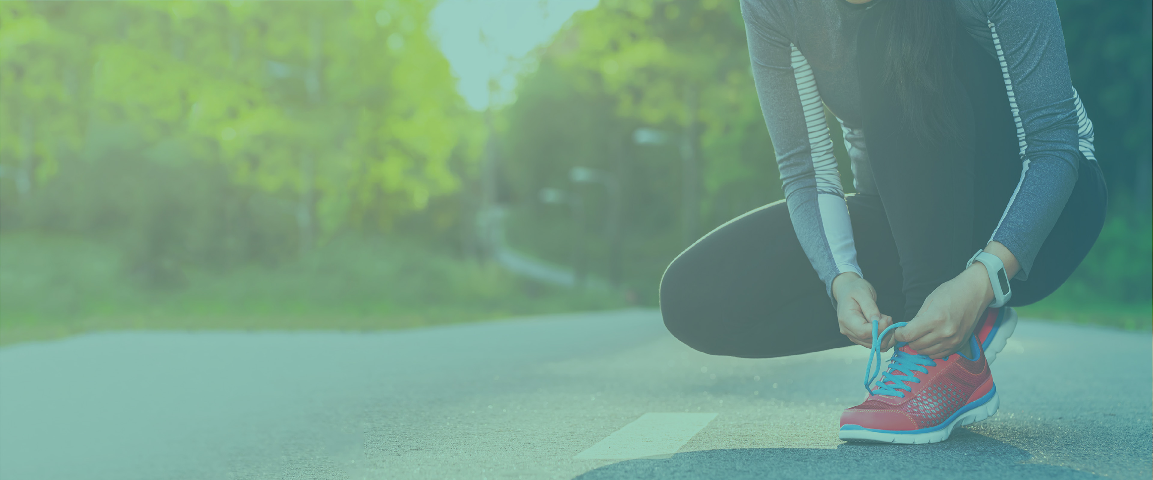 female runner squatting to tie her shoe in the road with a forest backdrop